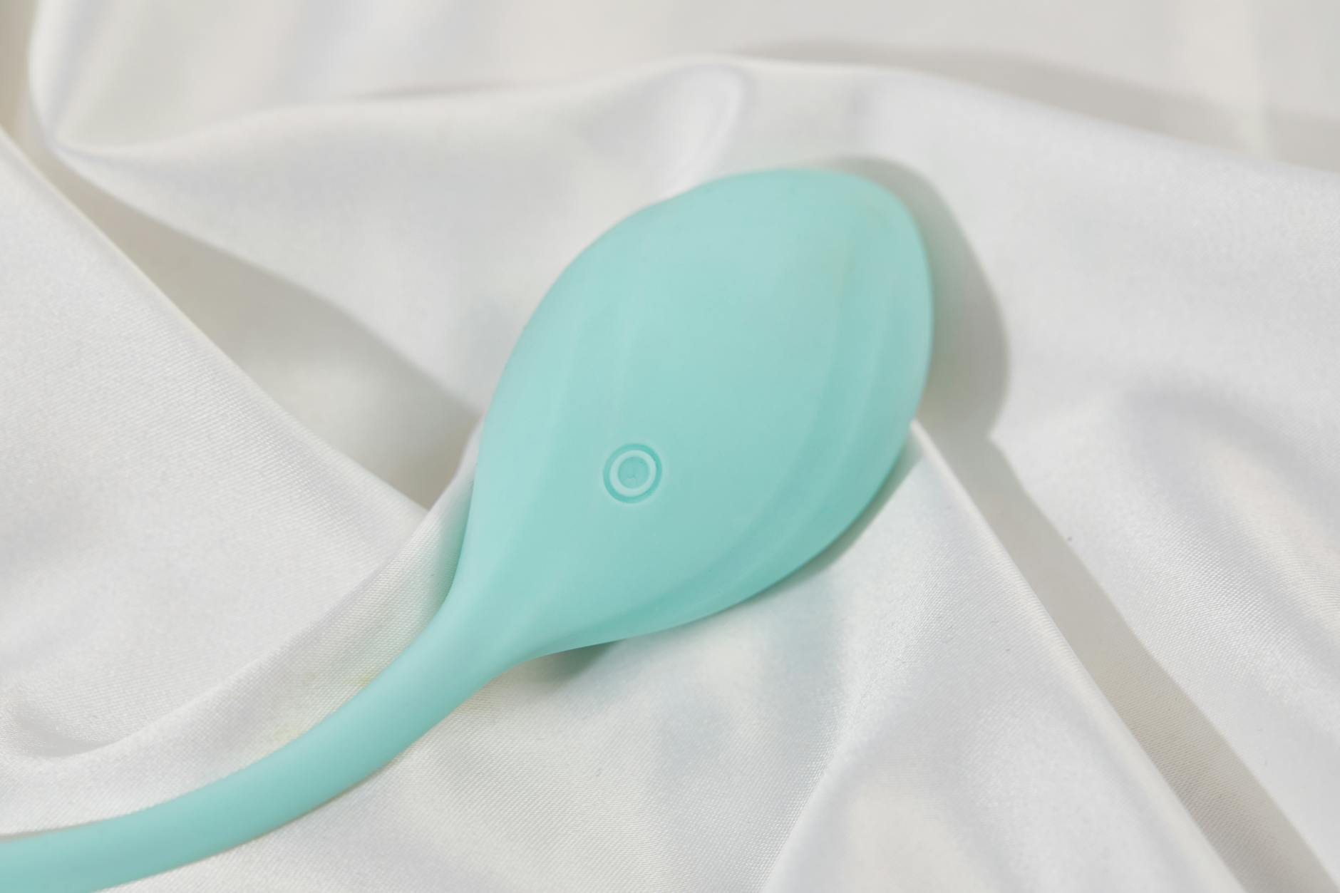 A sleek teal vibrator on white silk, representing modern clitoral pleasure technology