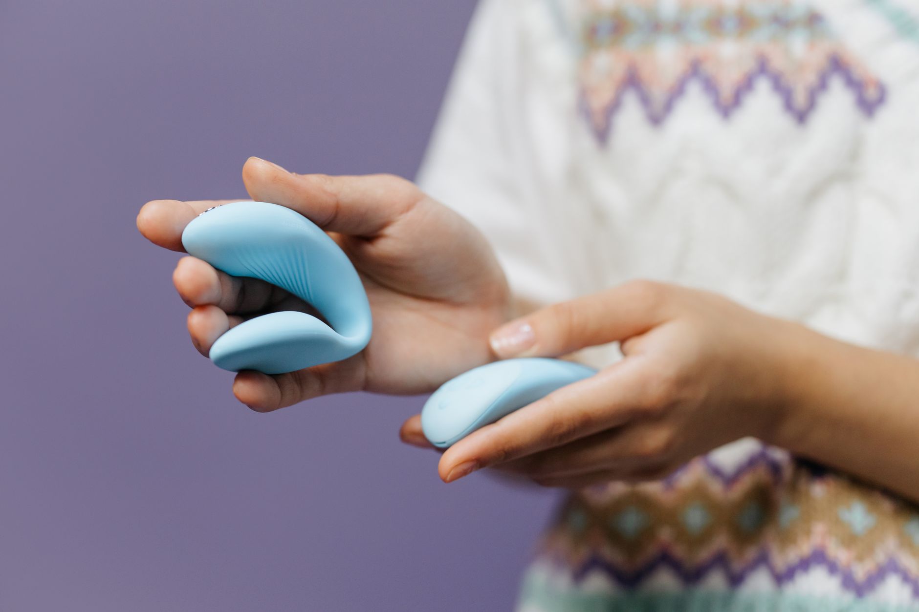 Hands holding a sleek blue vibrator against a purple background, representing slow, intentional pleasure.