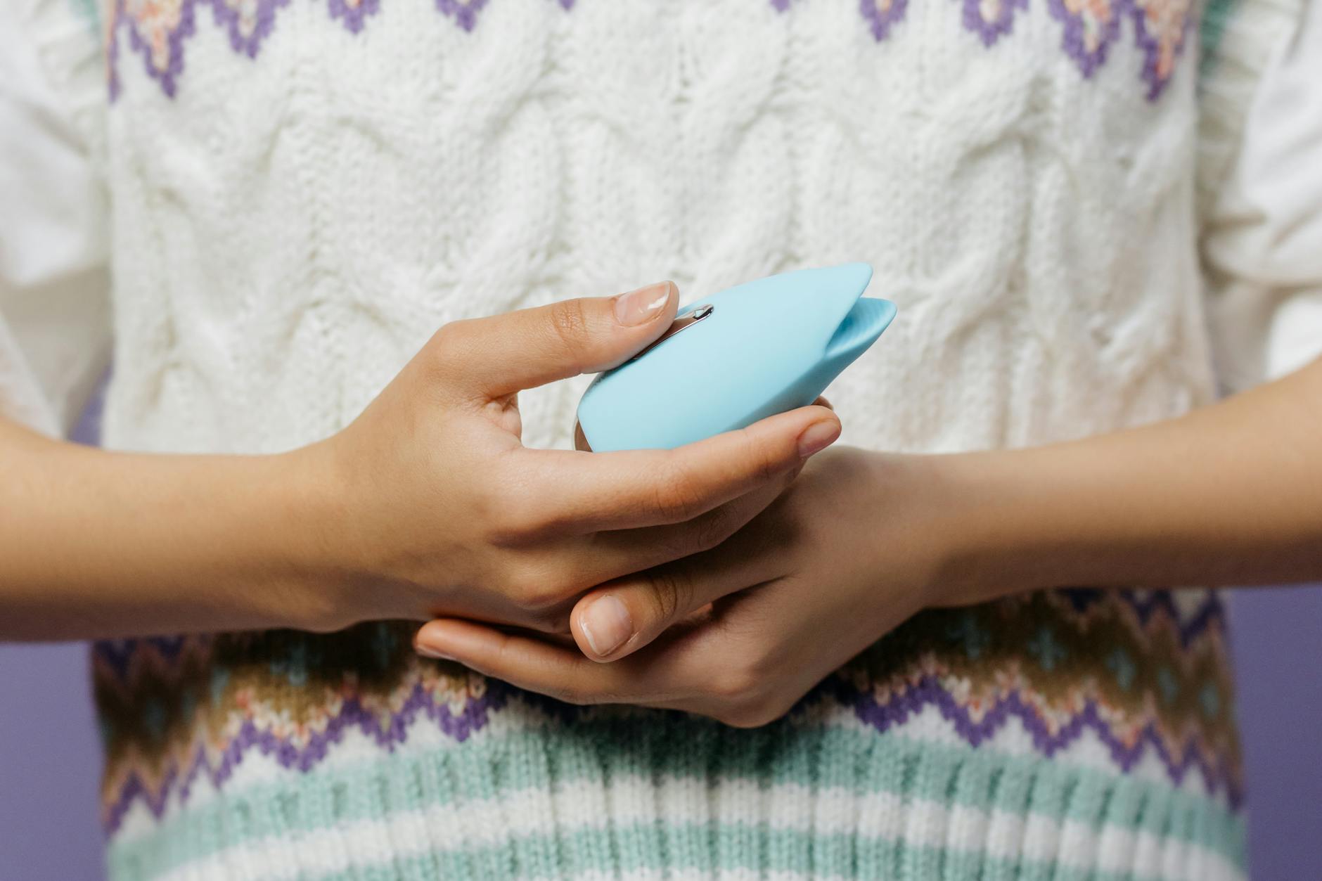 Hands holding a blue personal massager against a knitted sweater.
