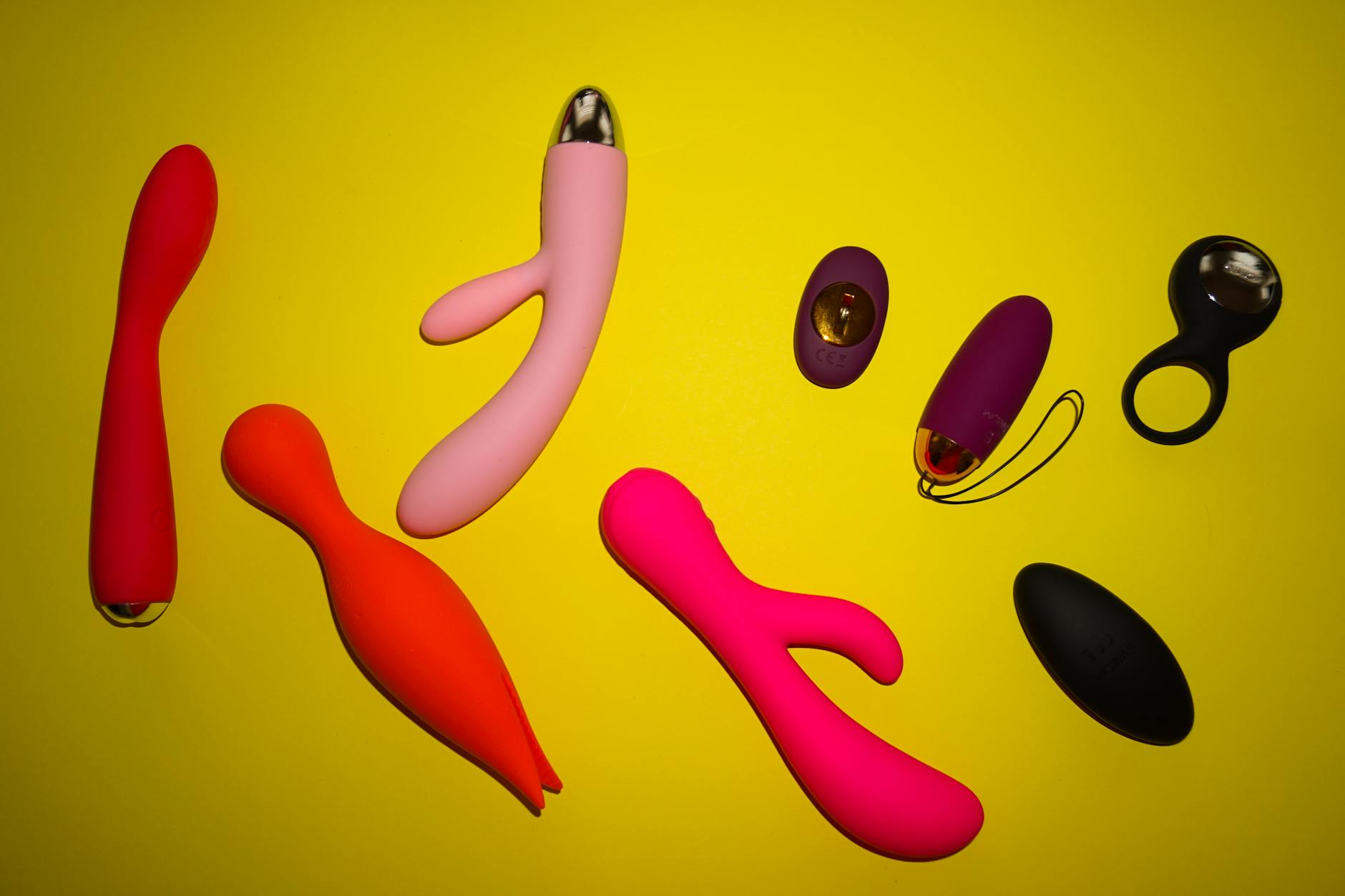 Close-up array of vibrant adult toys including vibrators in various colors against a neutral surface